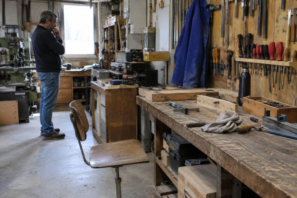 Un homme se tient debout dans un atelier près d'une fenêtre, entouré d'outils et d'établis